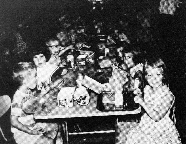 Black and white photograph of children seated at a cafeteria table eating lunch.